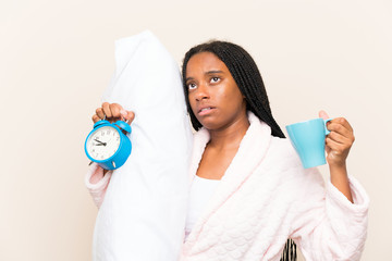 African American teenager girl with long braided hair in pajamas over isolated background and holding a cup of coffee