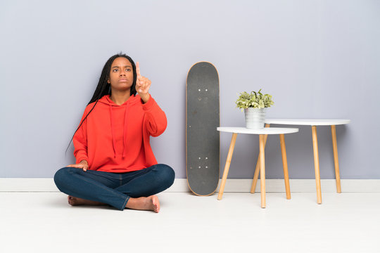 African American skater teenager girl with braided hair sitting on the floor touching on transparent screen
