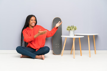 African American skater teenager girl with braided hair sitting on the floor extending hands to the side for inviting to come