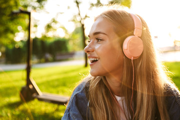 Girl outside in nature green park on grass listening music with earphones.