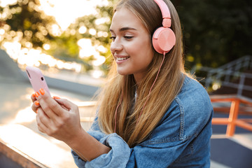 Positive young teenage girl outside in park holding mobile phone.