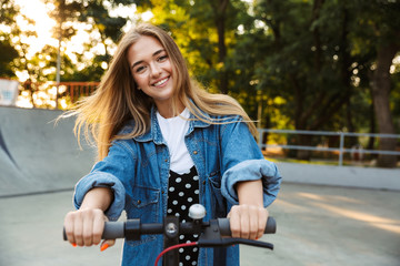 Smiling cheerful teenage girl in park walking on scooter.