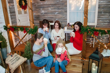 Several very pretty women and a teenager girl celebrate Christmas, the new year. Girls in the New Year's interior with cups in their hands look at each other, laugh, smile.
