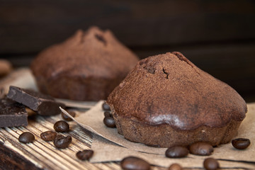 Homemade chocolate muffins on a wooden board with coffee beans and pieces of chocolate. Dark wooden background, closeup, selective focus
