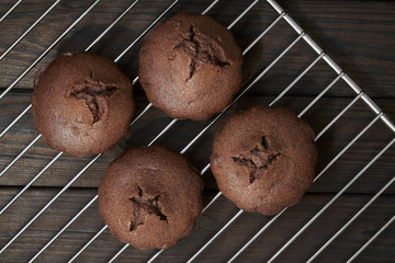 Homemade chocolate muffins on metal oven grill. Dark wooden background, top view
