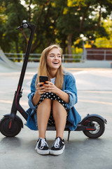 Happy teenage girl in park sit on scooter using mobile phone. © Drobot Dean