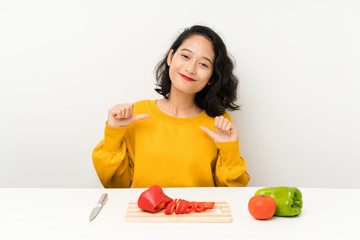 Young asian girl with vegetables in a table proud and self-satisfied