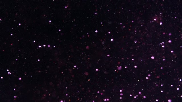 Glittering dark background suddenly filled out by numerous purple snowball bokeh lights falling from above.