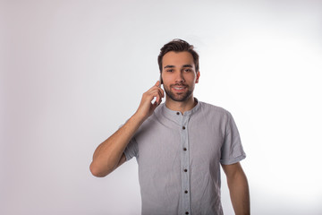 Portrait of a happy smiling bearded business man talking via mobile phone while standing isolated in studio against wall background with copy space for promotional content