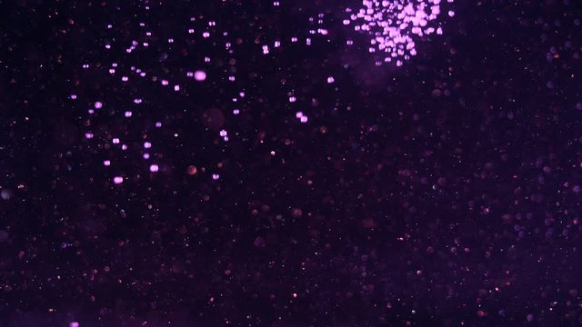 Glittering dark background suddenly filled out by numerous purple snowball bokeh lights falling from above.