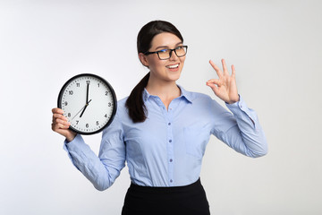Businesswoman Holding Clock Gesturing OK On White Studio Background
