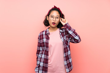 Naklejka premium Asian young woman over isolated pink background with glasses and surprised