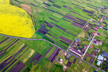 Fototapeta na wymiar Rural landscape on spring or summer day. Aerial view of green and plowed fields, village or town house roofs and roads on sunny dawn. Drone photography.