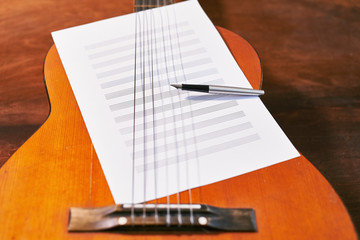 on the guitar are a white sheet with notes and a pen.