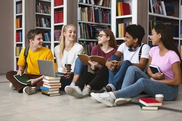 Classmates sitting on floor at library, chatting while studying