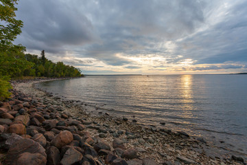 A rocky beachside near sunset on a very cloudy day. A boat floats in the distance