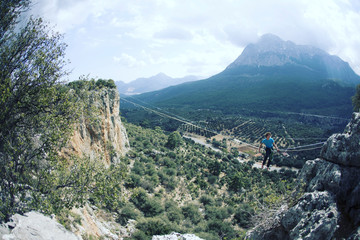 A man is walking along a stretched sling. Highline in the mountains. Man catches balance. Performance of a tightrope walker in nature. Highliner on the background of the mountains.
