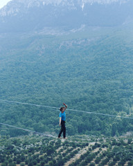 A man is walking along a stretched sling. Highline in the mountains. Man catches balance....