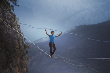 A man is walking along a stretched sling. Highline in the mountains. Man catches balance....