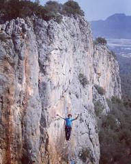 A man is walking along a stretched sling. Highline in the mountains. Man catches balance....