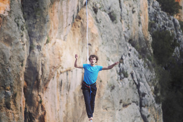A man is walking along a stretched sling. Highline in the mountains. Man catches balance....