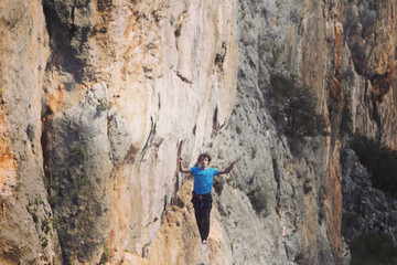 A man is walking along a stretched sling. Highline in the mountains. Man catches balance. Performance of a tightrope walker in nature. Highliner on the background of the mountains.