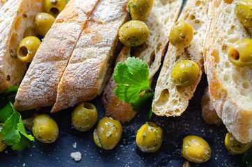 Baguette stuffed with olives, cut with fresh green olives and parsley, served on a stone plate