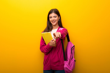 Teenager student girl on vibrant yellow background points finger at you