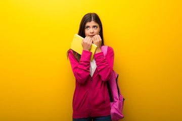 Teenager student girl on vibrant yellow background is a little bit nervous and scared
