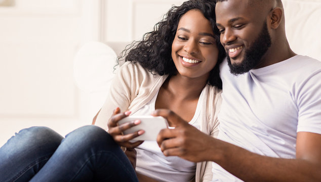 Happy african couple watching funny videos on smartphone at home
