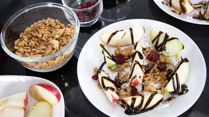 Healthy snack homemade: red and green apple, oat granola, whole grain and berries with chocolate syrup on top in a white bowl. Balanced diet and healthy eating concept.