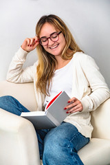 Happy woman reading book sitting on chair at home