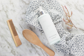 A bottle with shower gel a brush and a hair comb with a piece of fabric with flowers on a marble table