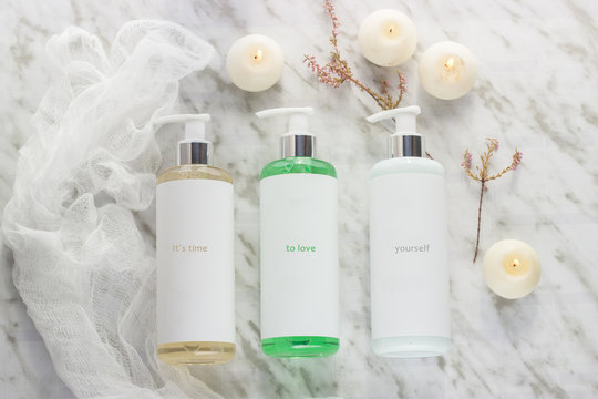 Three bottles with gel, champoo and cream with three candles and a piece of white chiffon on a marble table in a bathroom