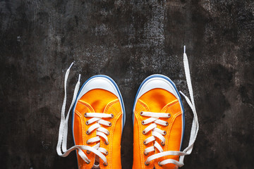 yellow-orange sneakers with untied laces on a dark concrete background. Copy space. View from above.