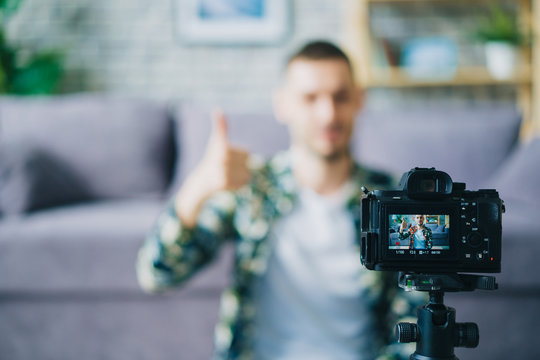 Close-up of digital camera recording modern blogger showing thumbs-up recording video in apartment, focus on equipment. People, technology and house concept.