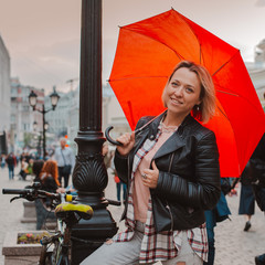 young cheerful woman under a red umbrella in the city center in autumn