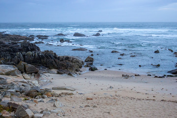 Atlantic Ocean coast in Portugal in the morning. Seascape in blue morning fog. Ocean beach with stones and waves. Empty beach. Rocky coastline. Calm ocean shore. Wild nature concept. 