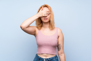 Young woman over isolated blue background covering eyes by hands. Do not want to see something