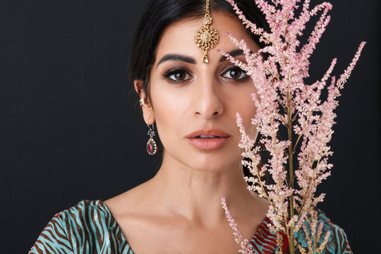 Image of beautiful hindus girl with makeup wearing traditional indian saree dress and ethnic jewelry holding flower branch