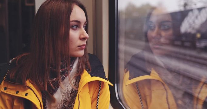Sad Young Woman Looking Out of a Train Window. SLOW MOTION 4K. Tired,  depressed girl thinking of something seating near the window in city train during her daily commute.