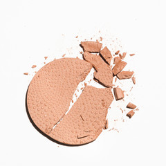 A makeup product, cracked in pieces on a white background