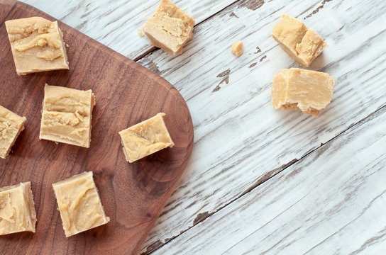 Squares of delicious, homemade peanut butter fudge over a rustic wood table background. Image shot from top view.