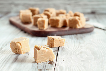 Squares of delicious, homemade peanut butter fudge over a rustic wood table. Selective focus on candy in the foreground with blurred background.