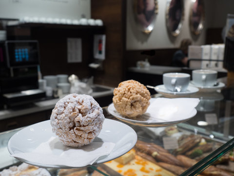 Close up of a Schneeballen cake with sugar on a plate on a glass shop counter top.Iconic of the town of Rothenburg. Another schneeball and cups of coffee are in background with deliberate blur - Image
