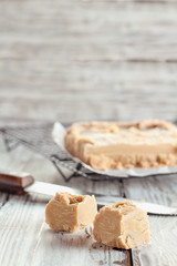 Squares of delicious, homemade peanut butter fudge over a rustic wood table. Selective focus on candy in the foreground with blurred background.