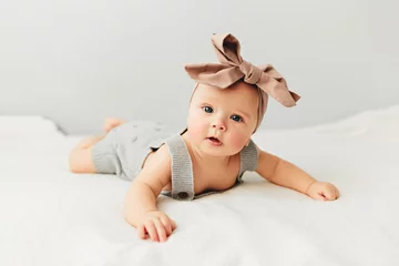 Fototapeten Beautiful baby lies on bed smiling bow on her head. © Vera