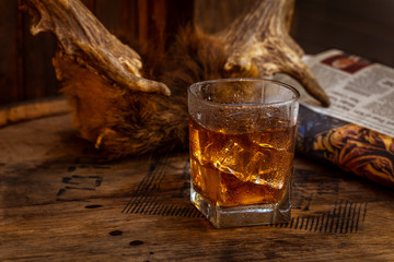 Glass of Whisky (whiskey), bourbon, ice tea or coke (cola) soda with ice and water drops on wood table and newspaper at dark background with copy space, close up