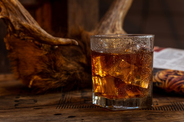 Glass of Whisky (whiskey), bourbon, ice tea or coke (cola) soda with ice and water drops on wood table and newspaper at dark background with copy space, close up