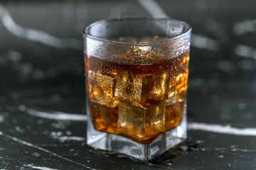 Glass of Whisky (whiskey), bourbon, ice tea or coke (cola) soda with ice and water drops on marble table, close up